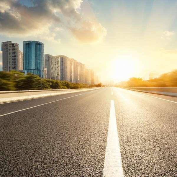 Straight road with sunrise in front heading towards a city with skyscrapers